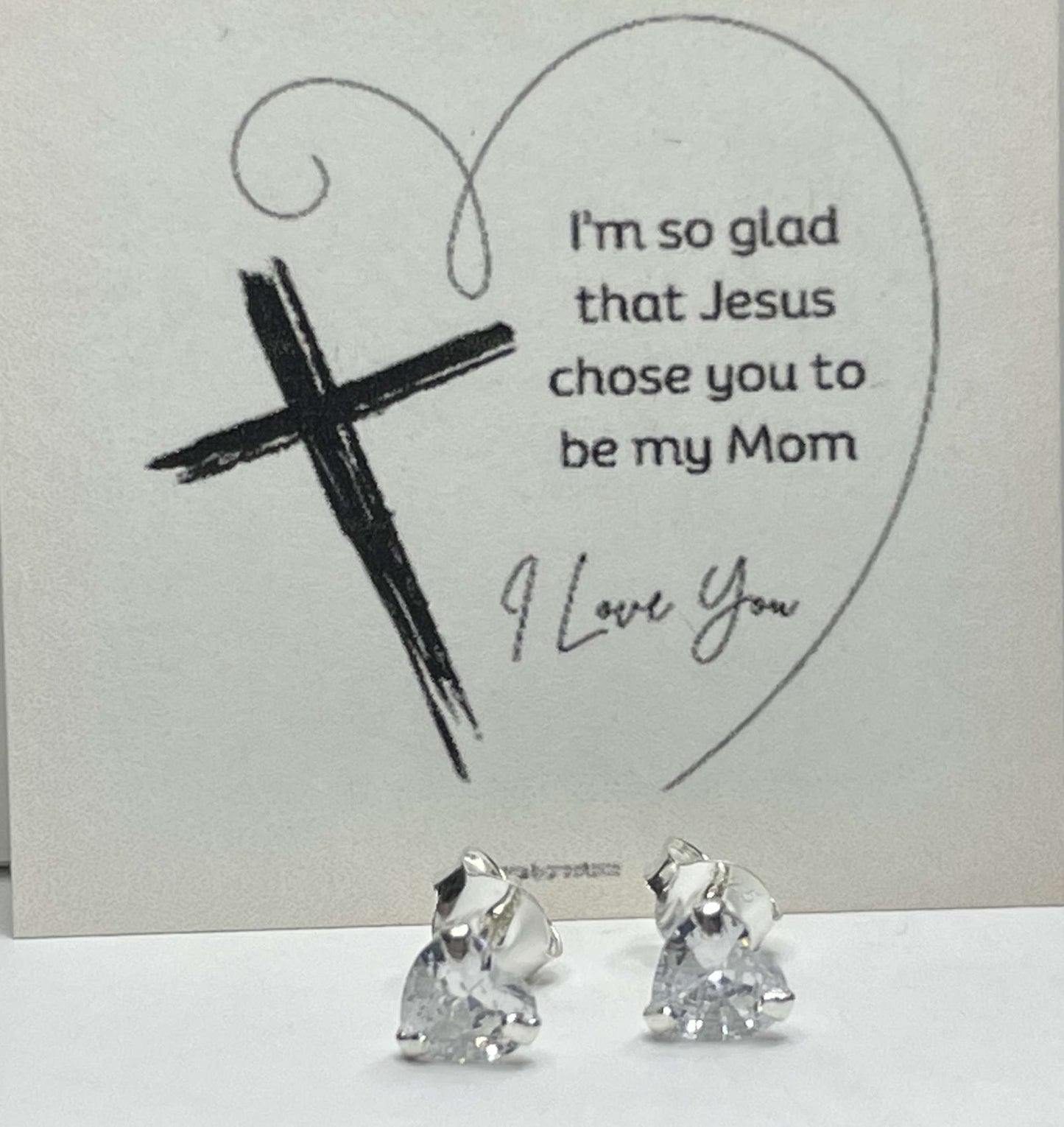 Silver heart stud earrings with CZ stones and religious card background.