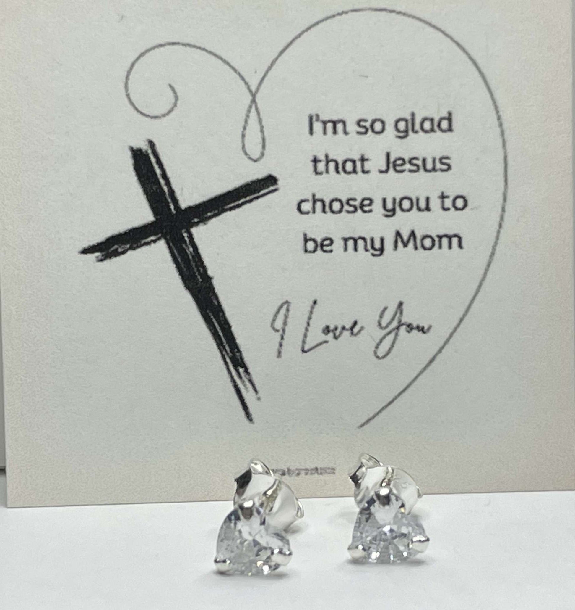 Silver heart stud earrings with CZ stones and religious card background.