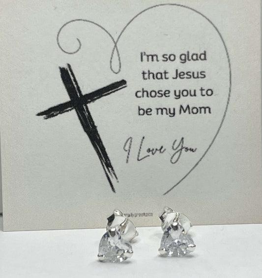 Silver heart stud earrings with CZ stones and religious card background.