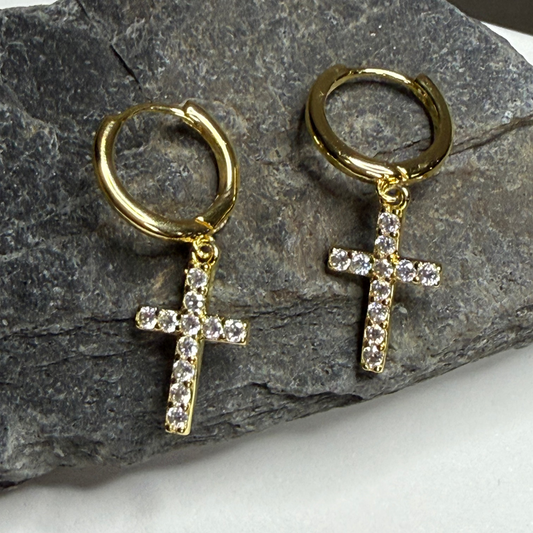 Gold hoop earrings with cross pendants on a stone surface