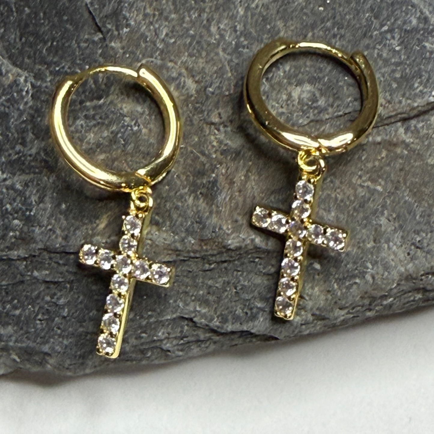 Gold hoop earrings with cross pendants on a stone surface
