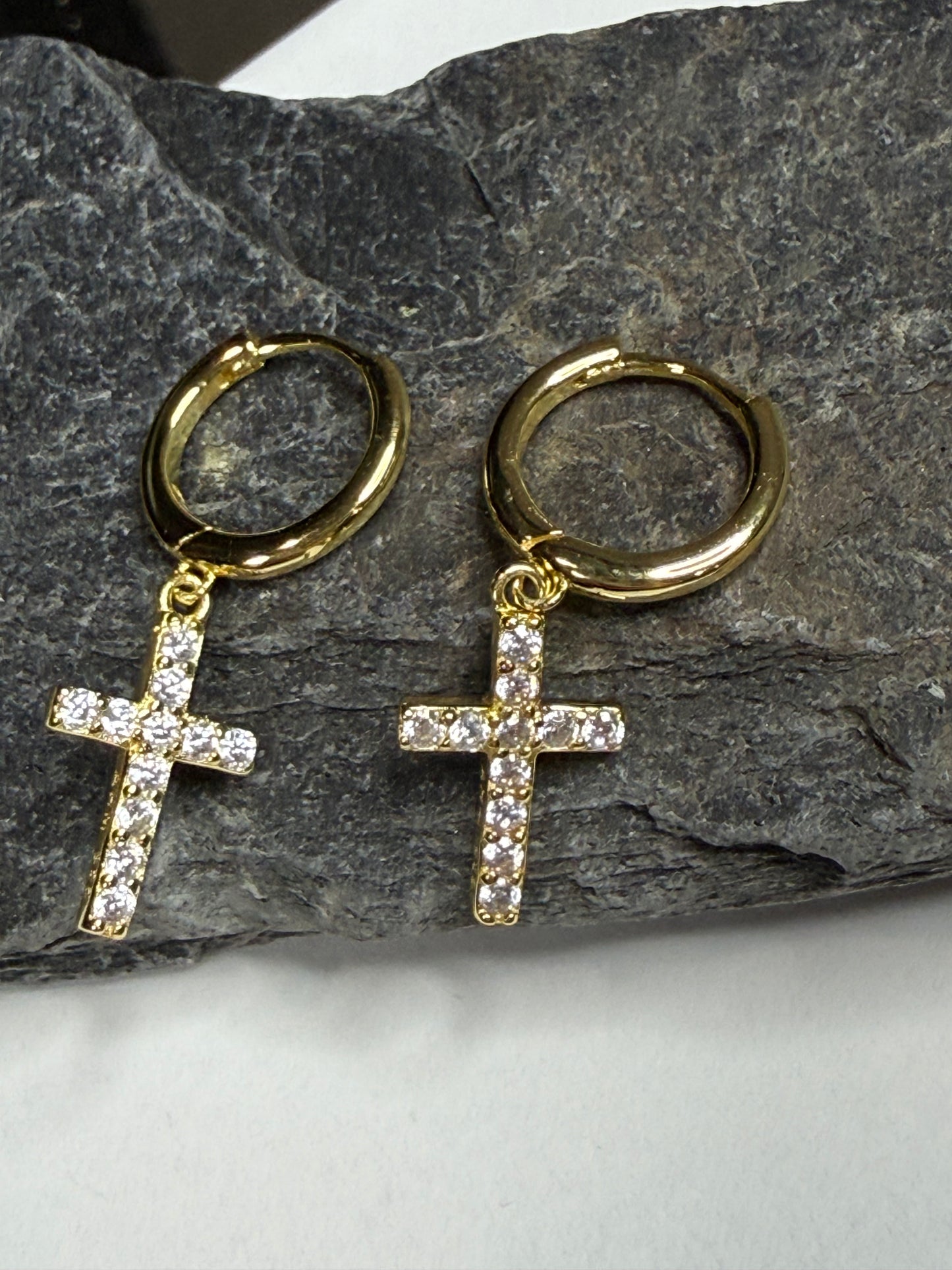 Gold hoop earrings with cross pendants on a stone surface