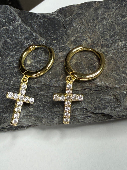 Gold hoop earrings with cross pendants on a stone surface
