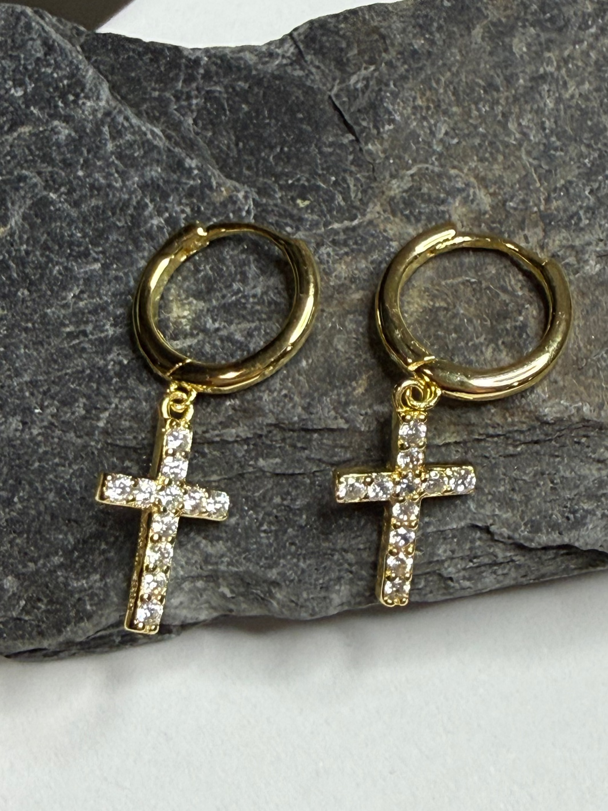 Gold hoop earrings with cross pendants on a stone surface